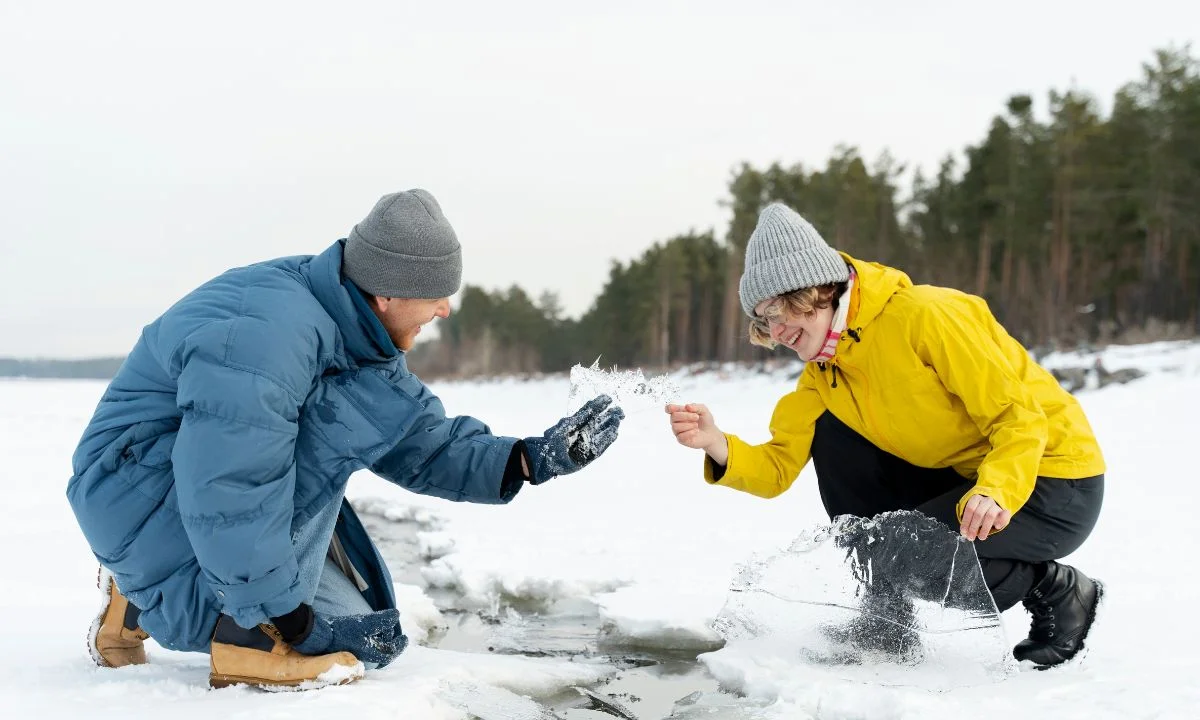 Two people wearing winter clothes, one in a blue jacket and the other in a yellow jacket, sharing pieces of ice on a frozen lake., Top 100+ Good Pick Up Lines to Break the Ice Smoothly